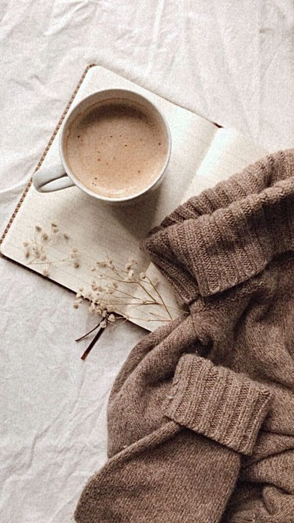 Cozy autumn scene with a warm cup of coffee, open notebook, and soft sweater on a textured background.
