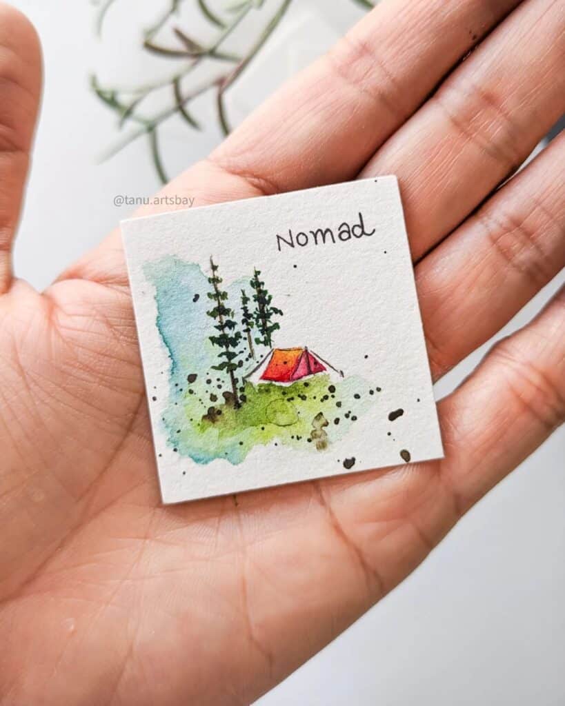Miniature watercolor art of a tent in nature, labeled Nomad, resting on a hand.