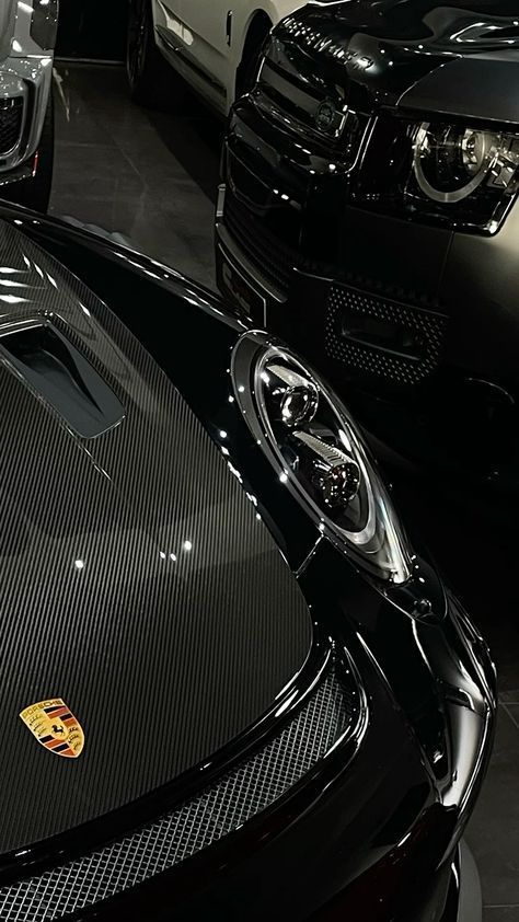 Luxury cars showroom featuring a sleek Porsche and stylish Range Rover in a dimly lit setting.