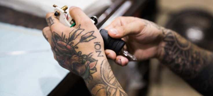 Tattoo artist with sleeve tattoos holding a tattoo machine, ready for inking. Hand tattoos