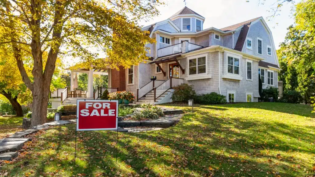 Charming two-story house for sale with autumn foliage and a For Sale sign on the front lawn.