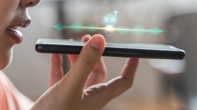 Person using voice command on smartphone with digital assistant icon and sound waves.