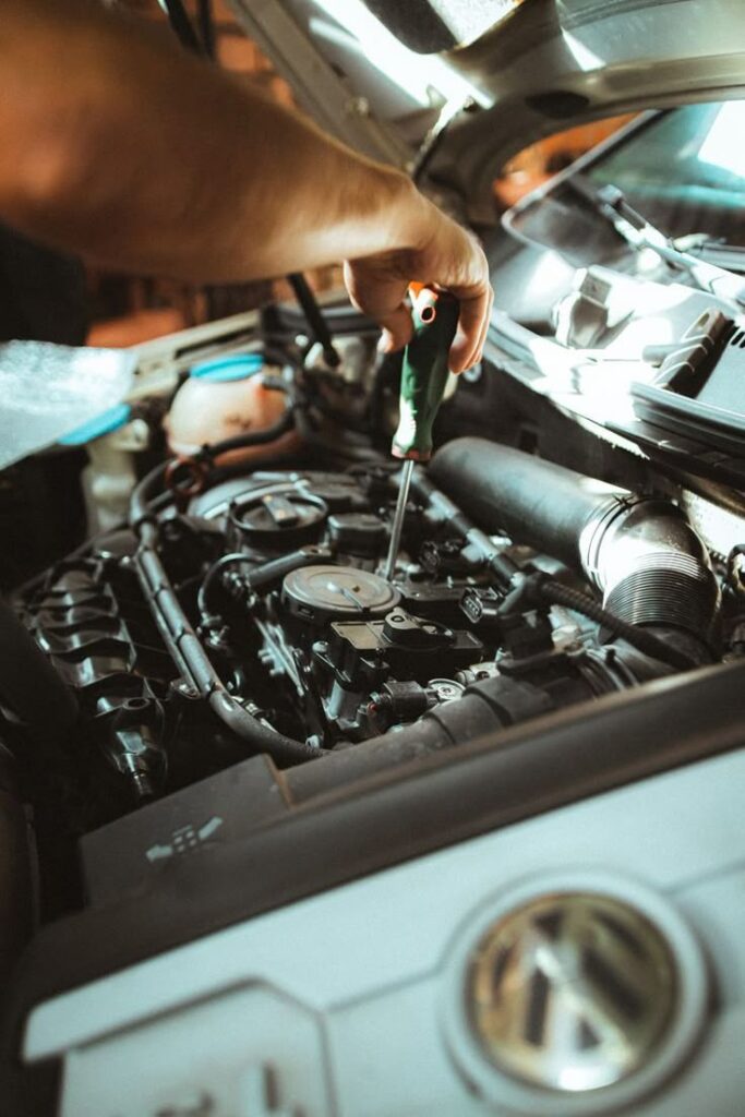 Mechanic using a screwdriver to repair a car engine under an open hood.