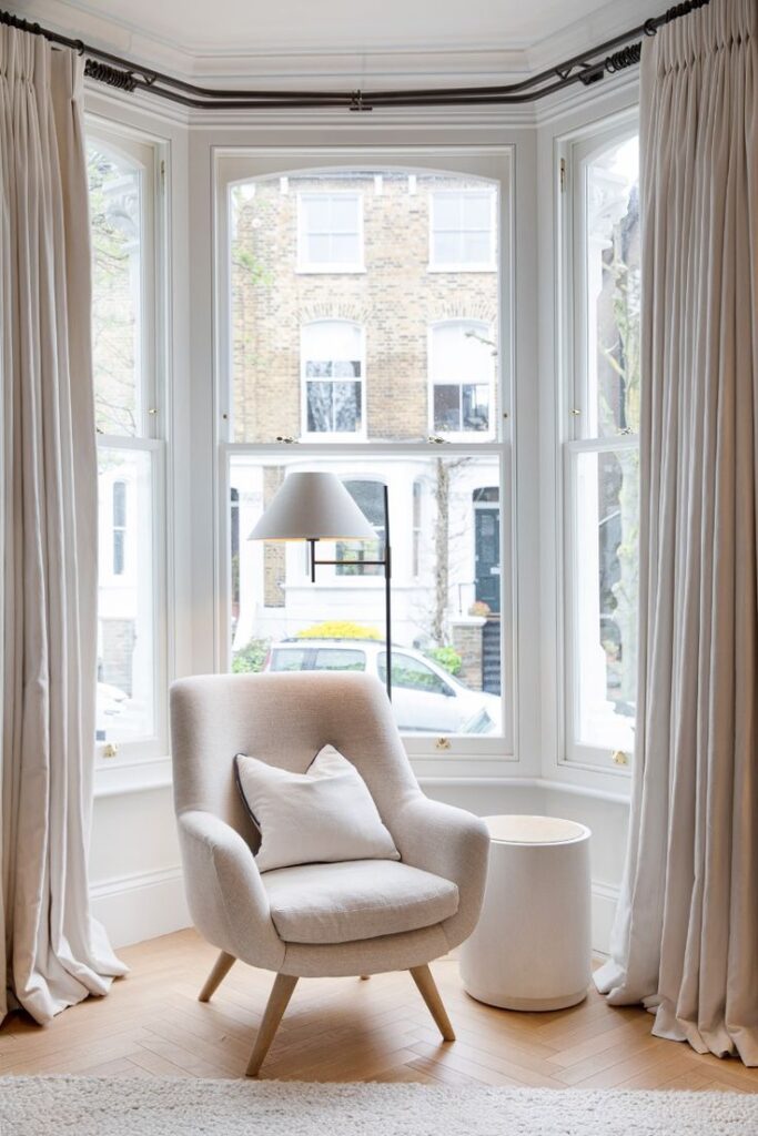 Cozy armchair with pillow near bright bay window and curtains in stylish living room.