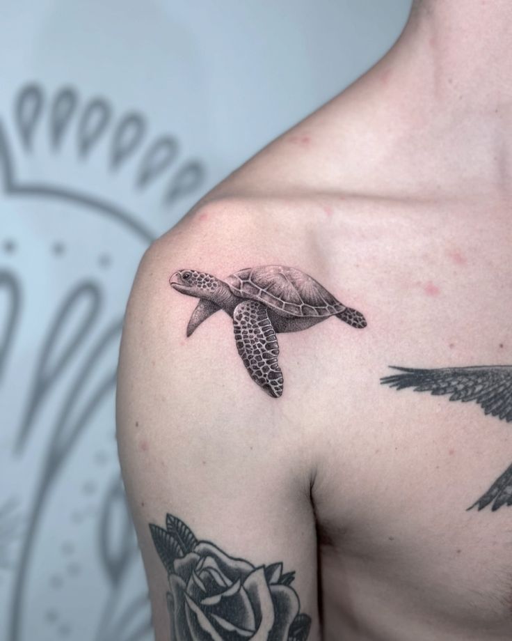 Sea turtle tattoo on upper shoulder, surrounded by floral and bird tattoos, with artistic black and gray shading.
