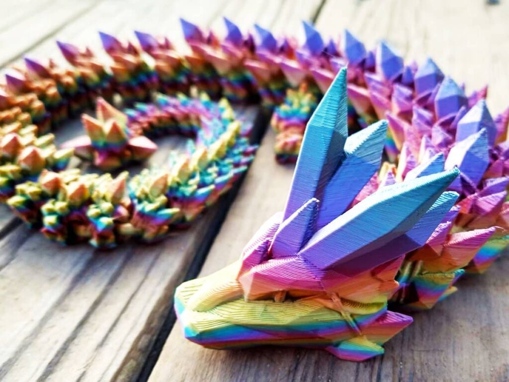 Vibrant 3D-printed rainbow dragon with intricate spikes coiled on a wooden surface.