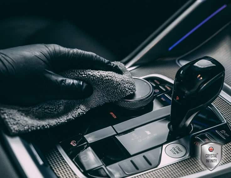 Cleaning a car's gear console with a microfiber cloth and glove, promoting interior vehicle detailing.