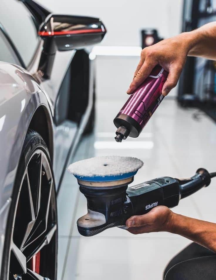 Car detailing in progress: hands applying polish to buffer near sleek vehicle for a glossy finish.