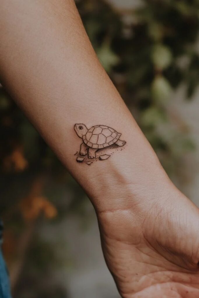 Minimalist turtle tattoo on forearm with blurred nature background.