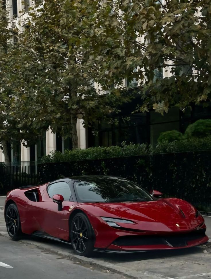 Sleek red sports car parked under lush trees on a city street, showcasing luxury and style.