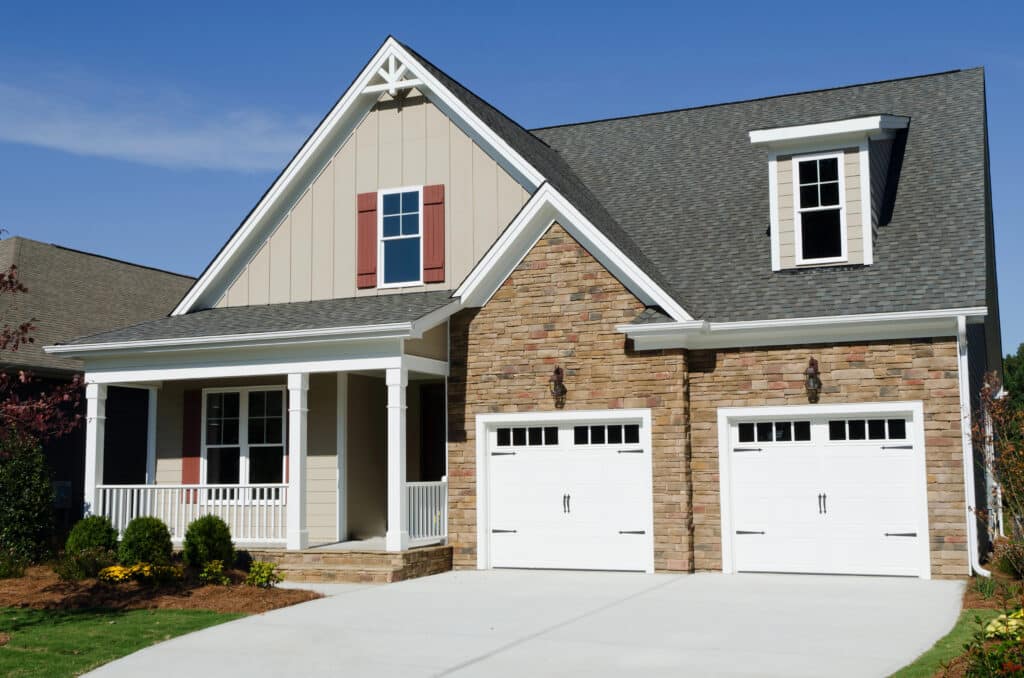Modern suburban house with stone facade, gable roof, and double garage under a clear blue sky.