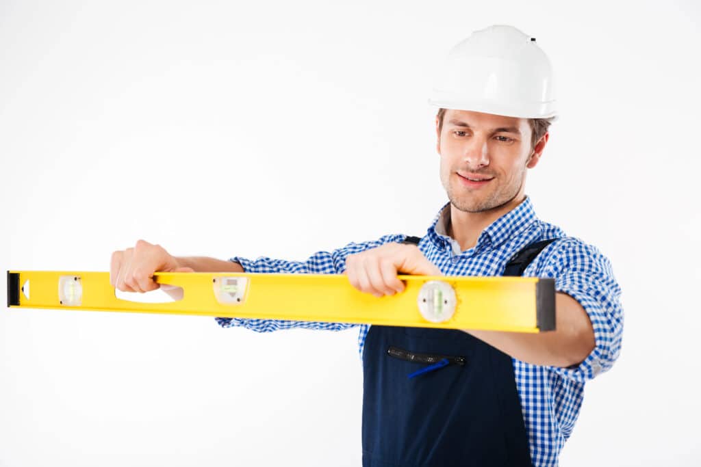 Construction worker using a yellow spirit level, wearing a hard hat and checkered shirt.