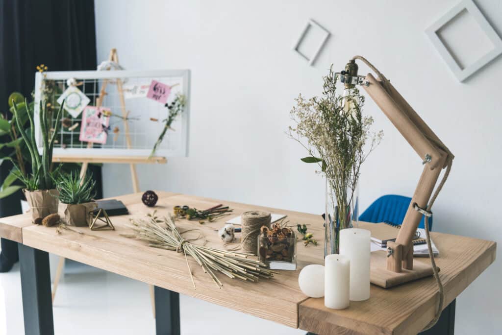 Decorative workspace with plants, candles, and crafting materials on a wooden desk, enhancing a creative atmosphere.