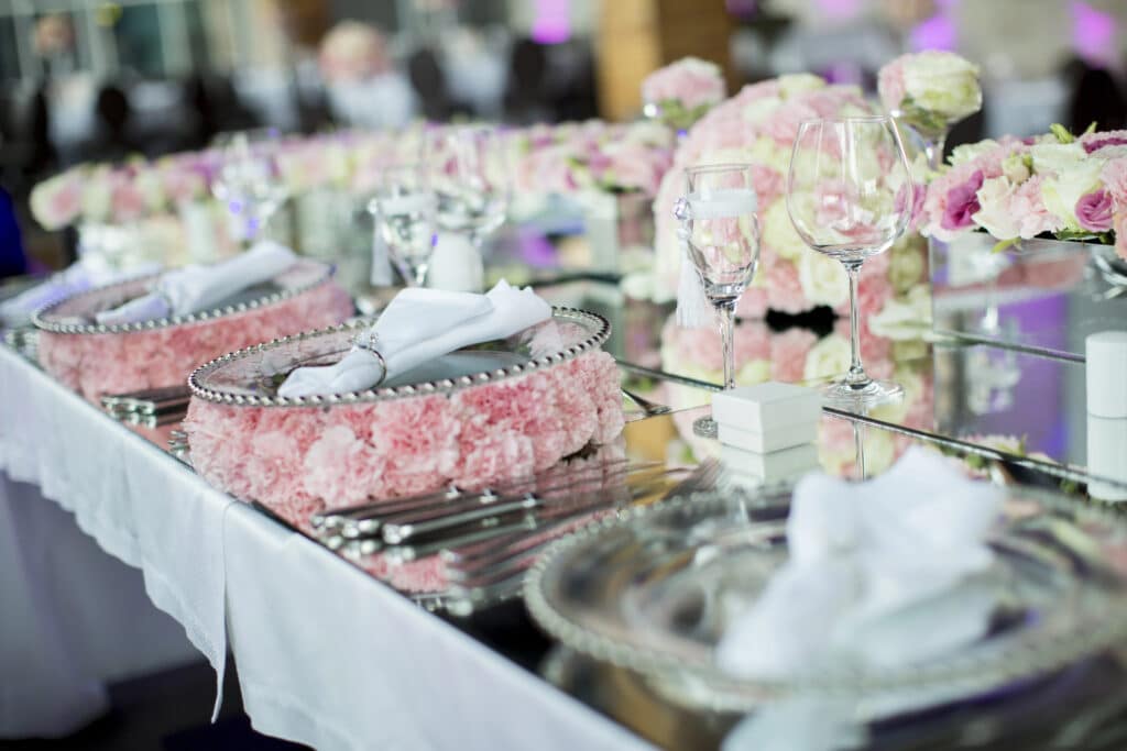 Elegant wedding table setting with pink floral decor, crystal glasses, and white napkins on silver plates.