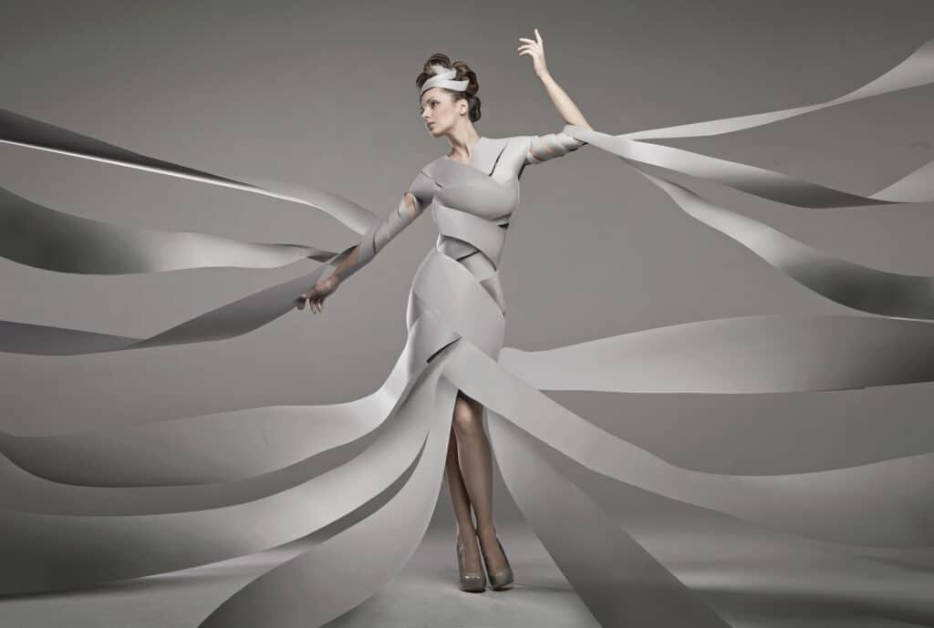 Depositphotos_17821245_L Artistic woman in flowing white dress made of ribbons, striking a dynamic pose against a gray background. | Sky Rye Design Artistic woman in flowing white dress made of ribbons, striking a dynamic pose against a gray background.