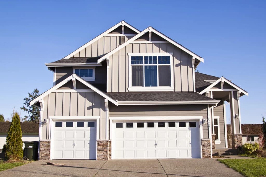 Modern two-story house with garage, gray siding, and large windows under a clear blue sky.