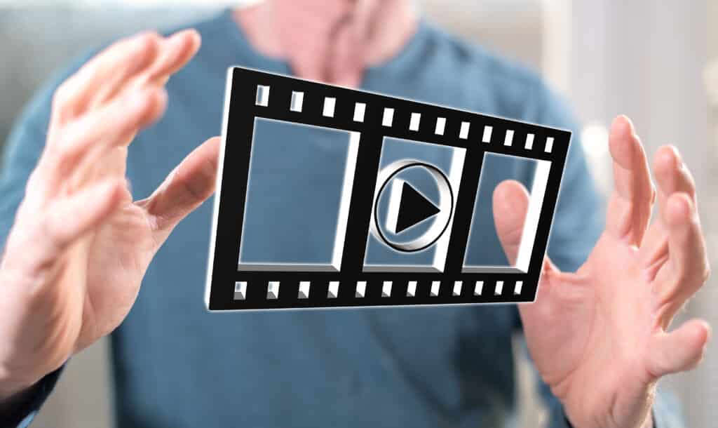 Person holding a virtual video play icon with a filmstrip design, symbolizing digital media and technology.