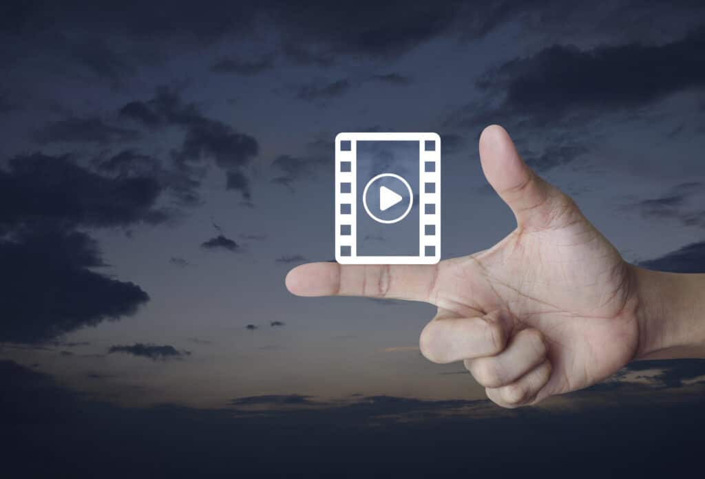 Hand gesturing a video icon against a cloudy sky, symbolizing creative media concept.