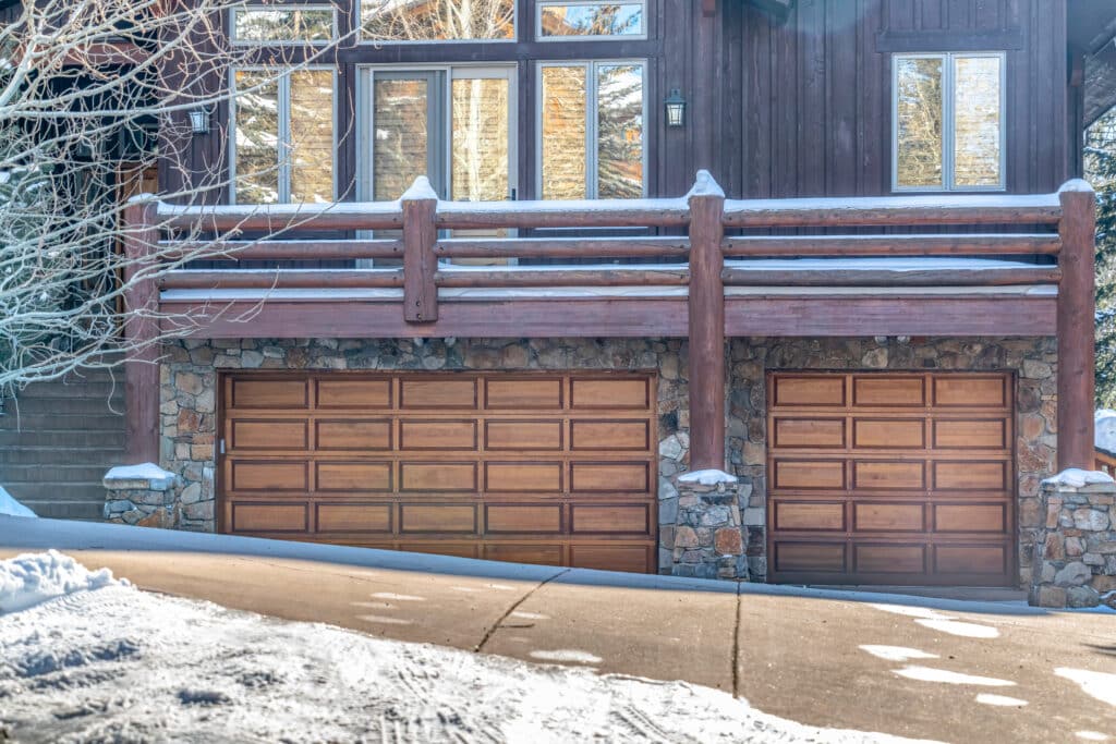 Snow-covered rustic wooden garage doors on a stone cabin in winter sunlight.