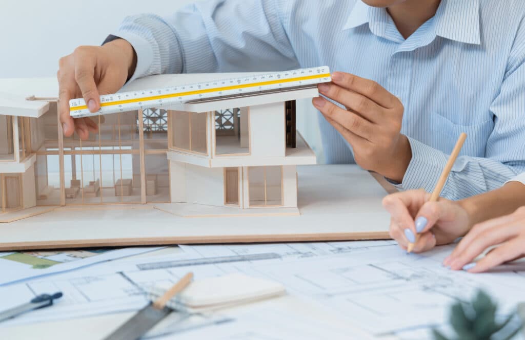 Architects measuring a scale model with blueprints in the background.