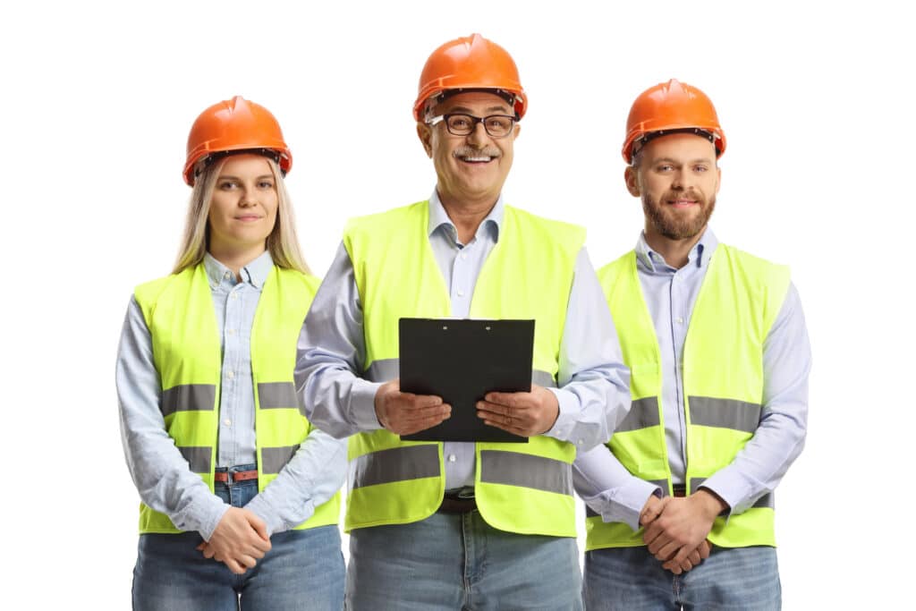 Three construction workers in safety vests and helmets, smiling and holding a clipboard.