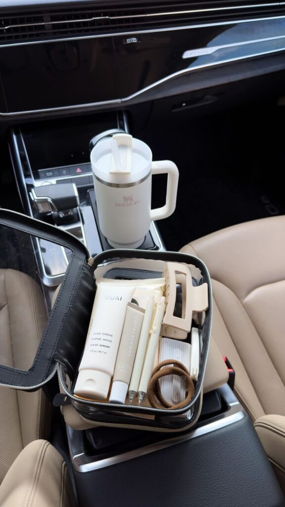 Travel kit with skincare and hair accessories on a car seat beside a white travel mug.