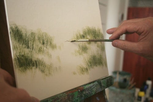 Artist painting green foliage on canvas with a brush, focusing on detail.