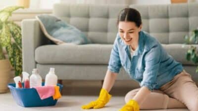 Woman cleaning floor with yellow gloves, using cleaning supplies, in cozy living room.