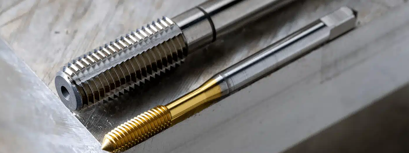 Metallic and gold-colored thread taps on a workbench, used for creating screw threads in metalworking.
