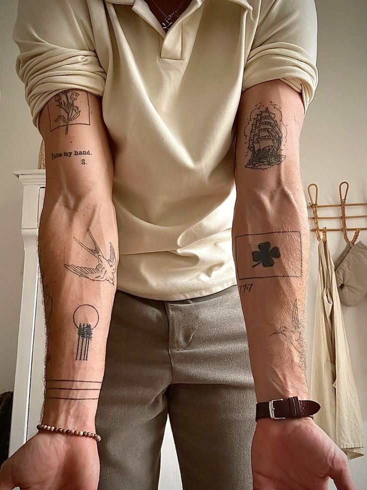 Person displaying forearm tattoos, including a ship, swallow, and geometric designs, with a casual shirt and brown pants.