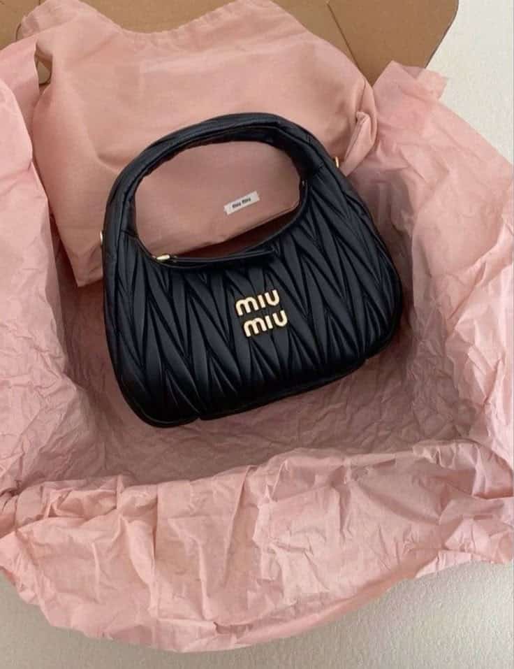 Luxury Miu Miu black handbag in pink tissue paper, showcasing elegant fashion packaging.