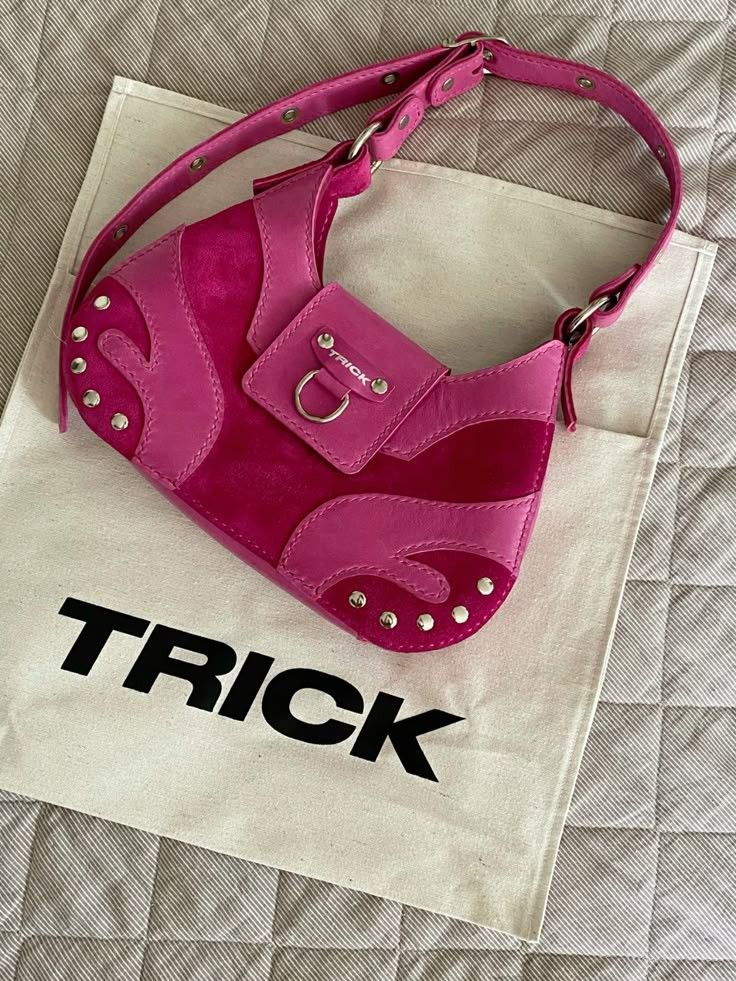Vibrant pink handbag with stud details on a beige TRICK branded cloth, placed on a quilted surface.