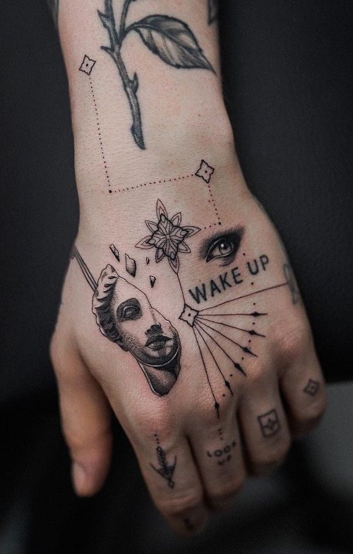 Tattooed hand featuring eye, face, geometric shapes, and WAKE UP text for artistic expression and body art inspiration.