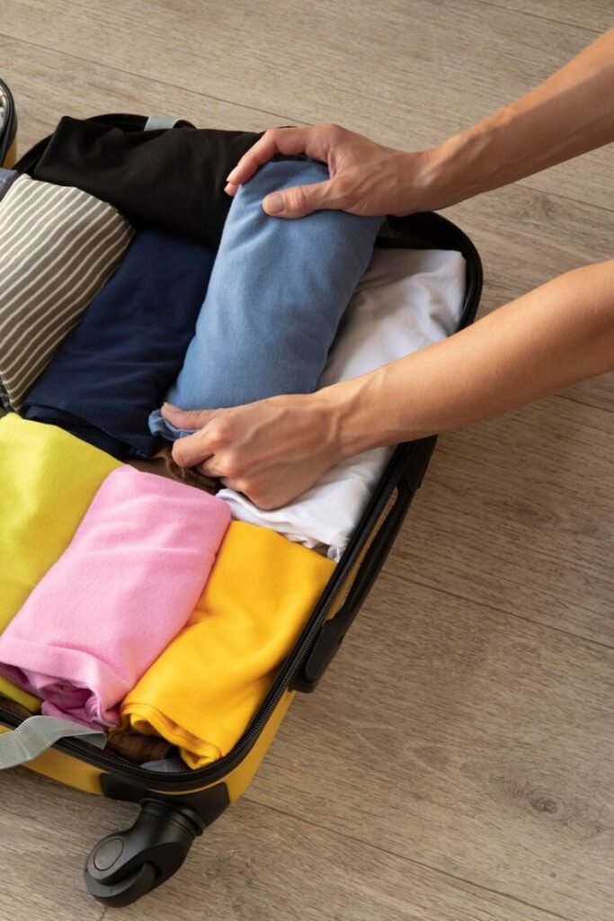 Packing neatly rolled clothes into a suitcase for travel on wooden floor background.