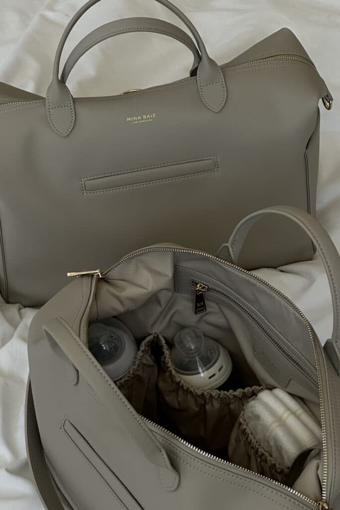 Gray diaper bag with baby bottles and essentials, showcasing organized storage on a light fabric background.