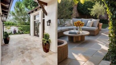 Stylish backyard patio with cozy seating, sunflowers on table, surrounded by lush greenery and elegant tiles.
