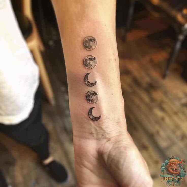 Moon phase tattoo on inner forearm, showing full and crescent moons in a vertical design, set in a tattoo studio.