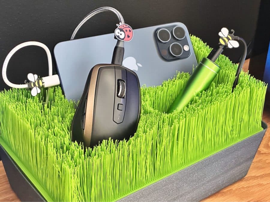 Grass-like organizer holding a smartphone, wireless mouse, and tech gadgets with cute insect cable holders.