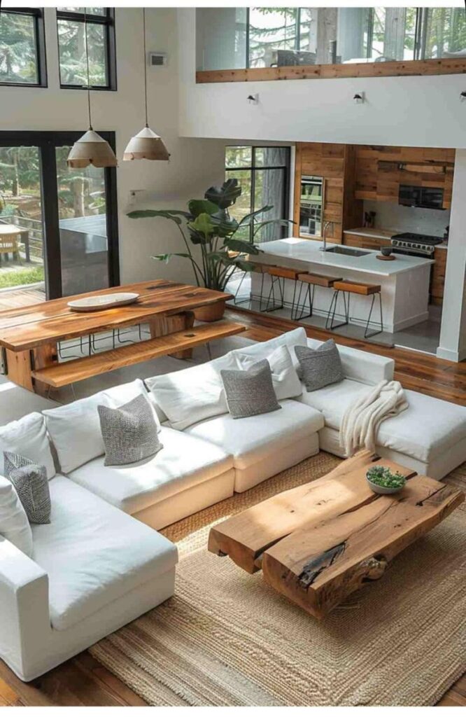 Modern open-concept living room with white sofa, wooden tables, kitchen island, and large windows.