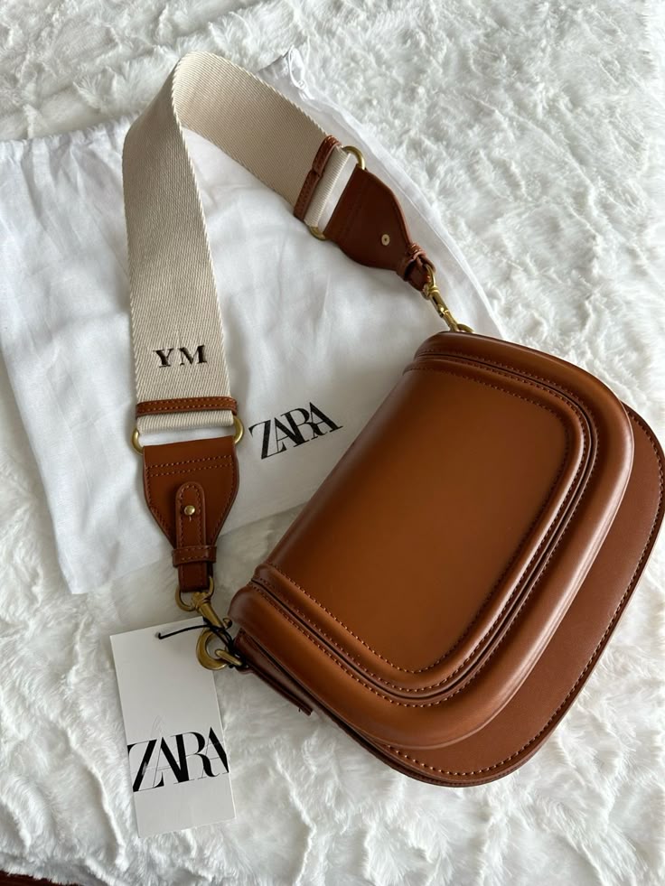 Brown leather Zara bag with adjustable strap, monogrammed “YM,” on a white surface for a stylish accessory display.