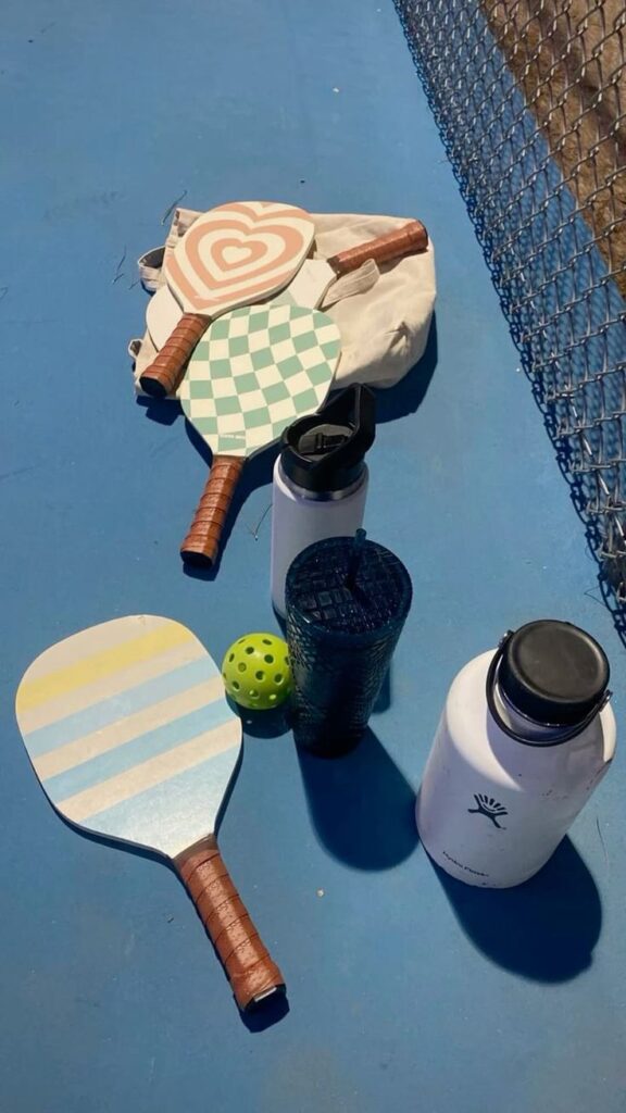 Colorful pickleball paddles, water bottles, and a ball on a court, ready for a fun game.