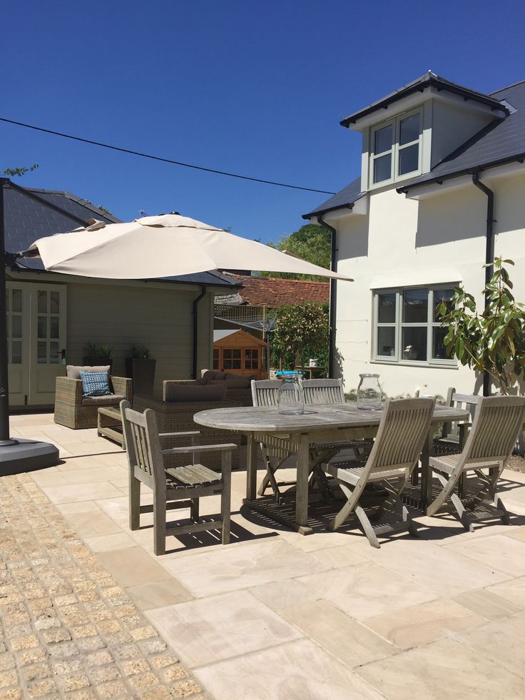 Spacious patio with outdoor dining set, umbrella, and cozy seating under a clear blue sky.