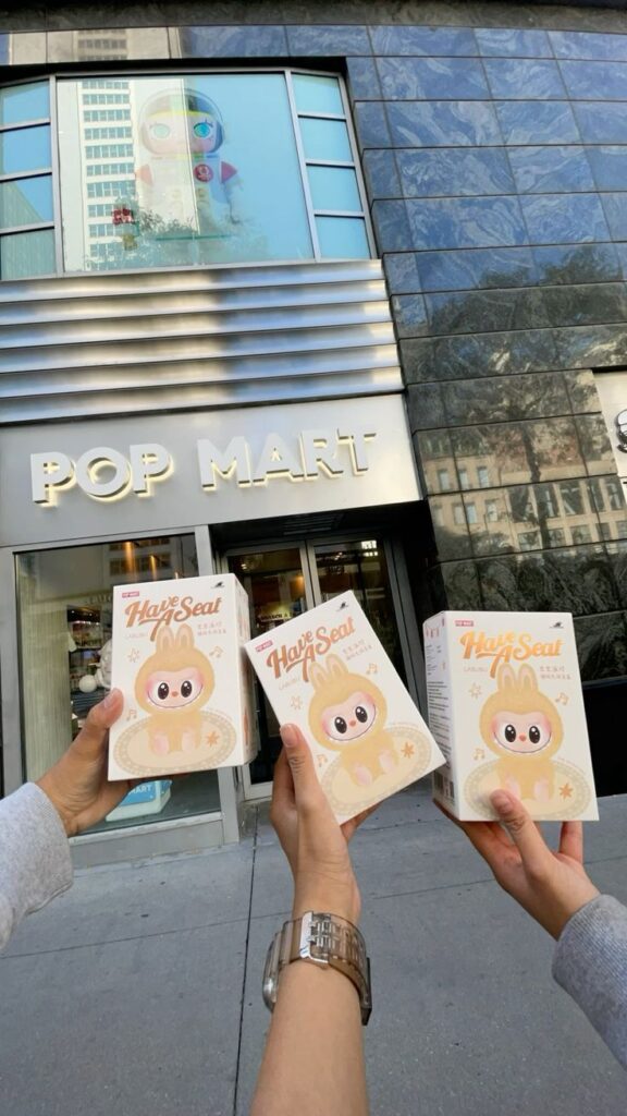 People holding collectible toy boxes in front of Pop Mart store entrance.