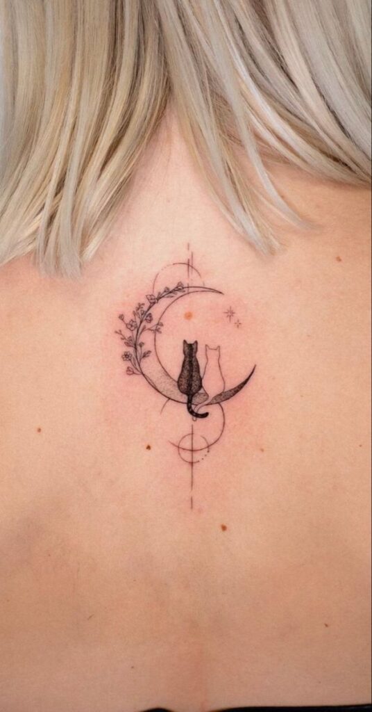Minimalist tattoo of two cats sitting on a crescent moon with floral and geometric designs.