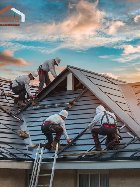 Roofers installing metal roof panels at sunset with vibrant sky background.