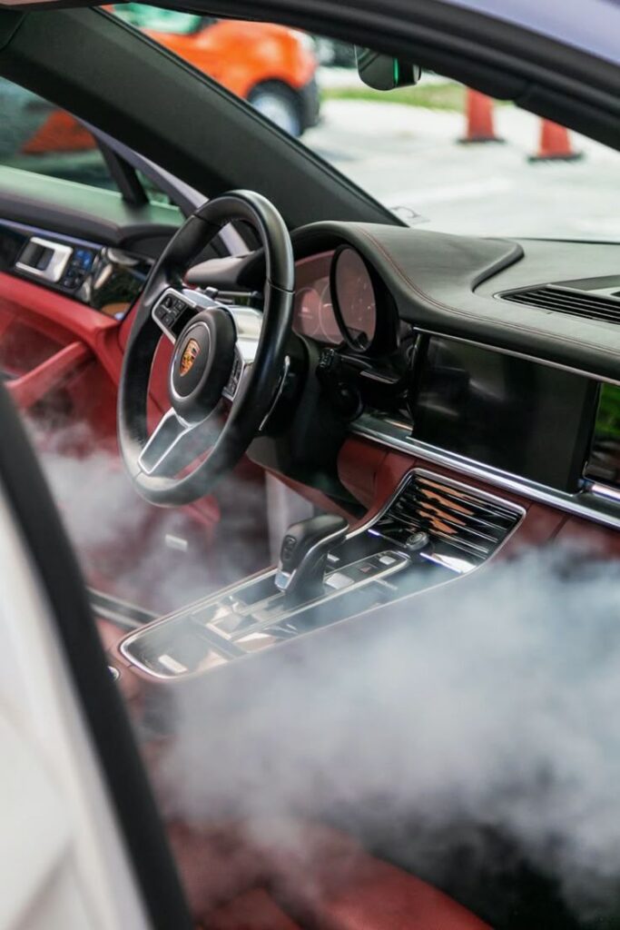 Luxury car interior with red leather seats and smoke effect, viewed from open door, sleek dashboard design.