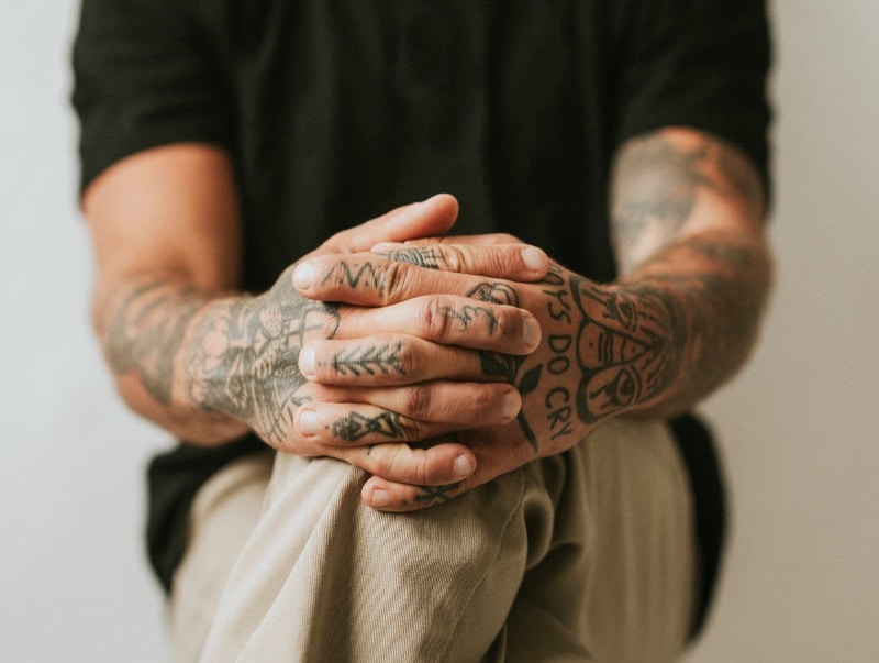 Tattooed arms and hands in a relaxed, crossed position, showcasing intricate ink designs.