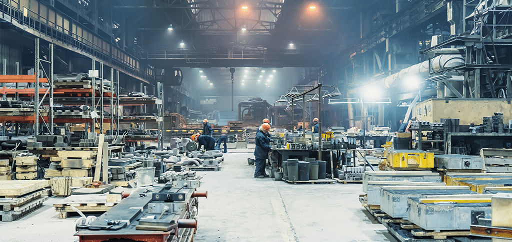 Workers in a spacious, well-lit factory with industrial equipment and shelving, showcasing a bustling manufacturing environment.