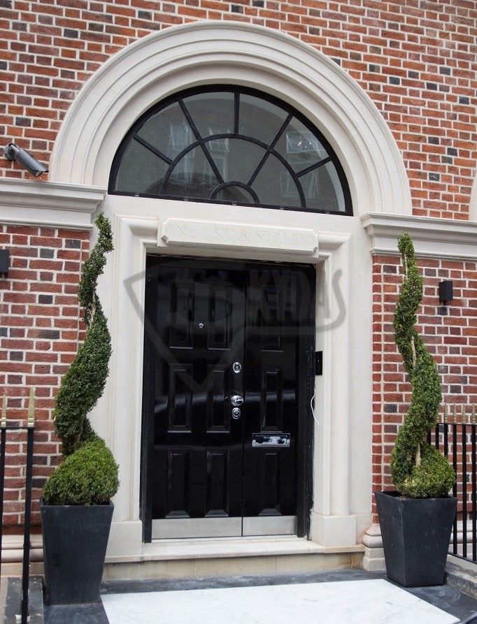 Elegant black front door with arch window and spiral topiary plants against a brick wall.