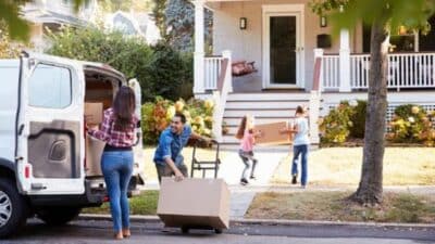 Family moving into new home, unloading boxes from a van, and carrying them inside.